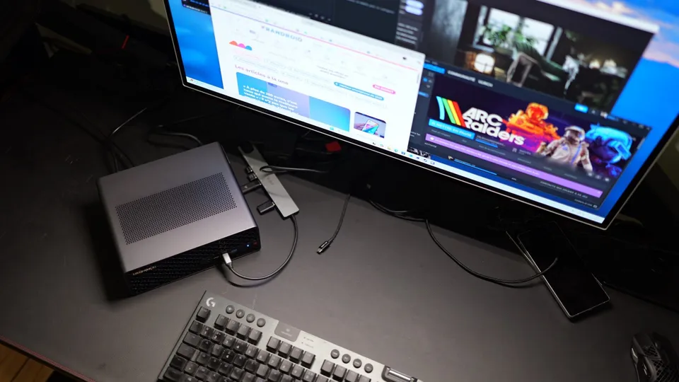 Minisforum MS-S1 Max, boîtier gris métal posé sur un bureau sombre au pied d'un écran et d'un clavier
